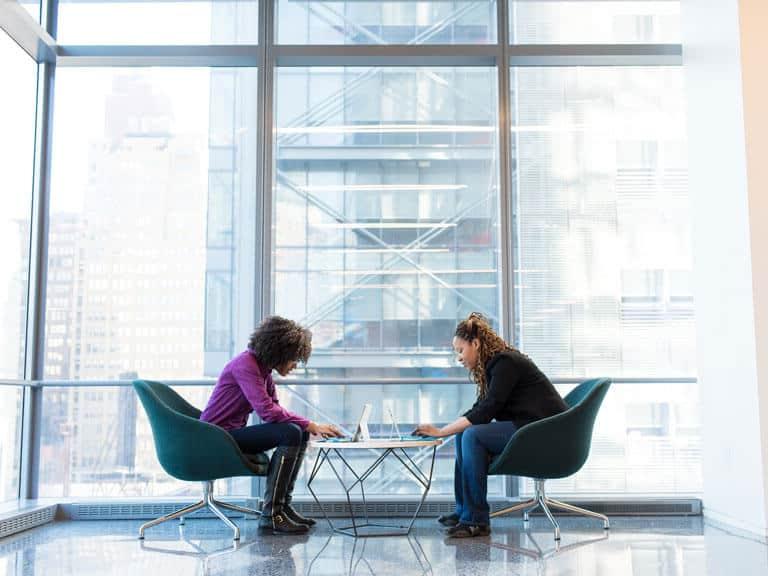 Two women work on laptops in hybrid work environment